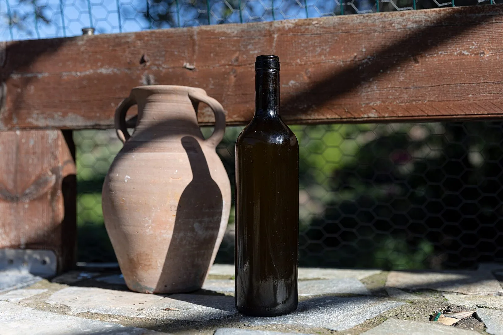 Una bottiglia di olio d'oliva accanto a un'anfora di terracotta
